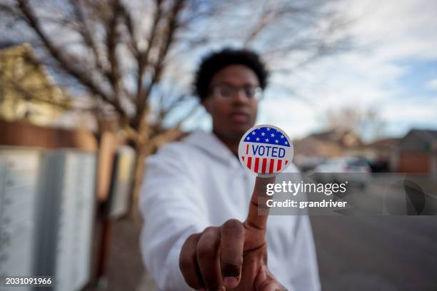 young african american man in his twenties holding an i voted sticker up to the camera and smiling - rösta bildbanksfoton och bilder