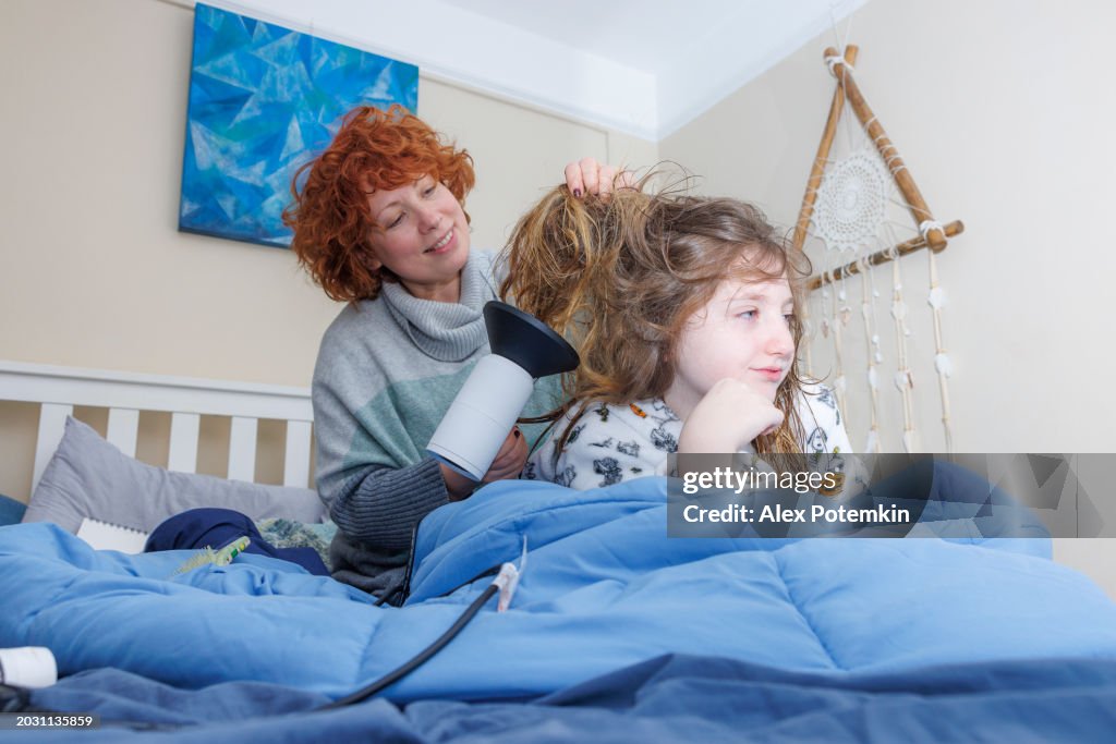 Child hairstyle and blow-drying on Halloween Eve. Mother drying thick long hair of her daughter in bed