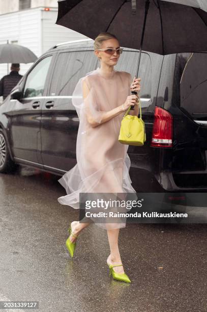 Leonie Hanne wears a sheer beige dress, green high heels, brown sunglasses, and a green Prada bag outside Prada during the Milan Fashion Week -...