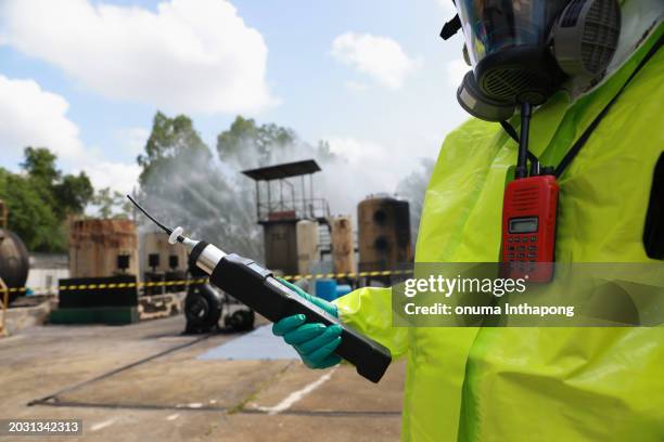 the male in a gas mask and hazmat suit holds the toxic air detector in a chemically polluted environment and danger zone - hazardous area sign stock pictures, royalty-free photos & images