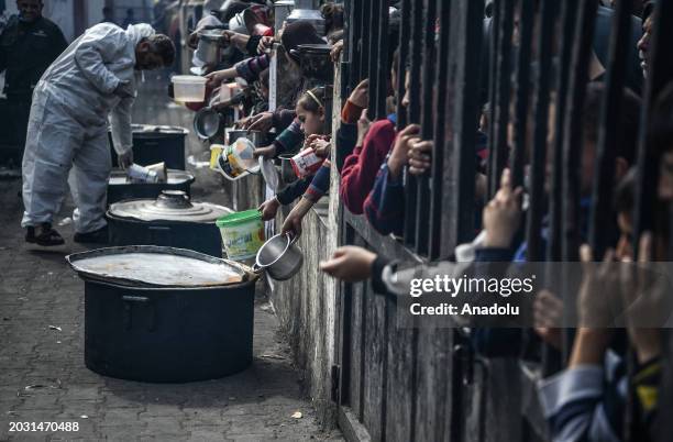 Palestinians hold out their empty containers to be filled with food, distributed by charity organizations, behind bars since they are unable to...