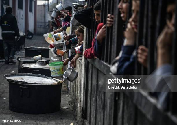 Palestinians hold out their empty containers to be filled with food, distributed by charity organizations, behind bars since they are unable to...