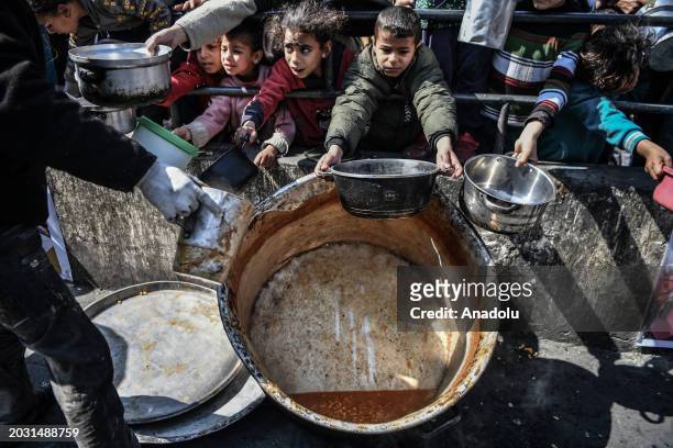 Palestinians hold out their empty containers to be filled with food, distributed by charity organizations, behind bars since they are unable to...