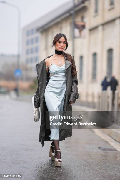 Heart Evangelista wears a black choker, a khaki long leather coat, a low neck blue gathered lustrous shiny satin midi dress, tights, platform bronze...