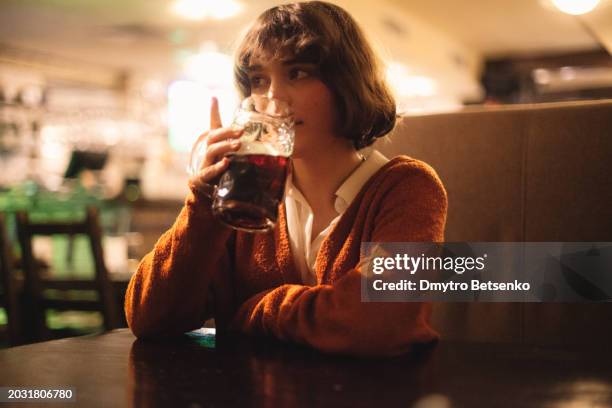 portrait of cute young woman drinking beer while sitting in the pub - ale stockfoto's en -beelden