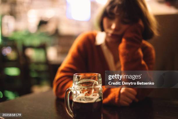 young woman sitting in the pub with beer glass standing on the table, soft focus - drunk stockfoto's en -beelden