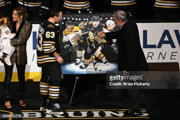 Brad Marchand of the Boston Bruins looks at a painting with president Cam Neely during a ceremony for playing in 1,000 NHL games before a game...
