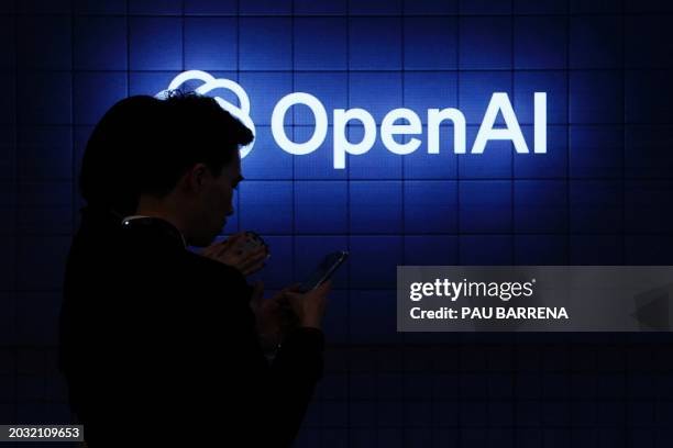 Visitor look at their phone next to an Open AI's logo during the Mobile World Congress , the telecom industry's biggest annual gathering, in...