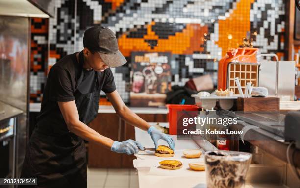 man, burger and fast food kitchen worker at counter with gloves, cooking and uniform at small business. restaurant, sandwich and cook with hamburger patty stack for lunch service with take away. - franchising stockfoto's en -beelden