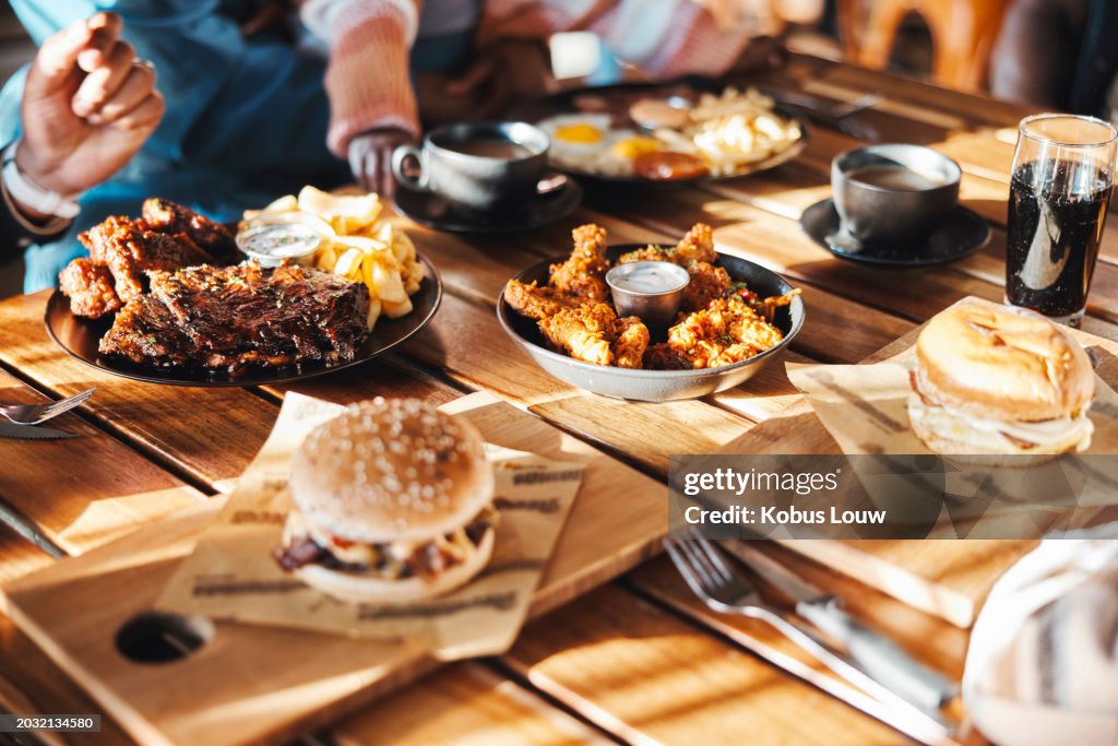 Fast food, lunch or dinner on table at restaurant, people eating for nutrition and wellness with time together. Catering, hospitality and cuisine with burger, chicken and ribs for protein at diner