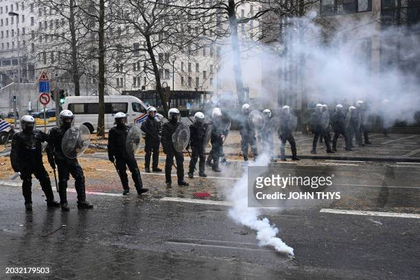 Belgian riot police officers stand guard as gas leaks from a tear gas canister during a protest called by the farmers' organizations "Federation Unie...