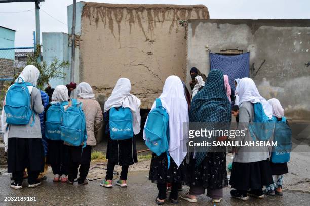 Afghan girl students carrying school bags observe rainwater collected in a canal along a roadside in Kandahar on February 26 2024.