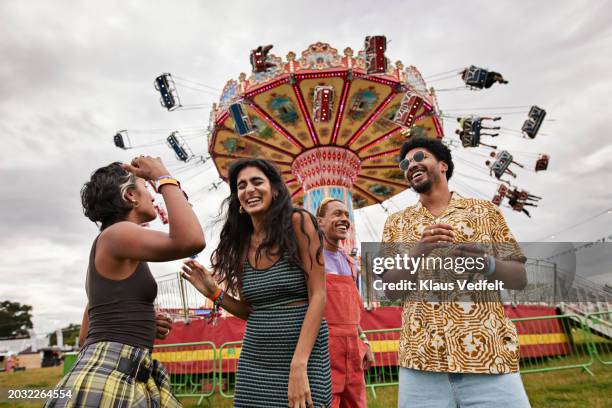 cheerful friends standing against chain swing ride - festival goer stock pictures, royalty-free photos & images