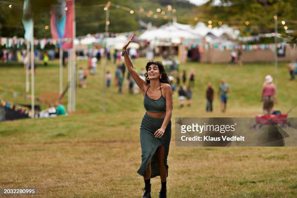 excited woman with raised hand walking at park - festivaleiro - fotografias e filmes do acervo