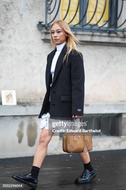 Guest wears white turtleneck top, a black oversized blazer jacket , a white mini skirt with floral details, a brown leather rectangular Prada bag,...