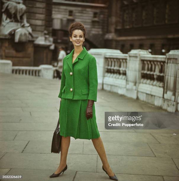 Female fashion model posed wearing a bright green wool suit featuring a single breasted jacket and pleated A line skirt, she stands at the top of a...