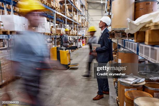 inspector pensativo entre los trabajadores manuales en movimiento borroso en el almacén. - proveedores fotografías e imágenes de stock