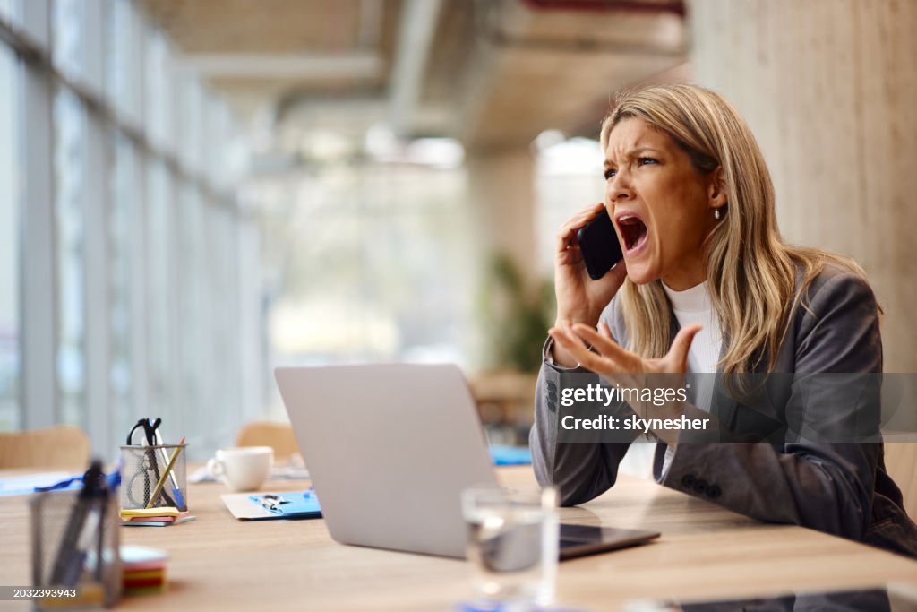 Angry businesswoman talking on mobile phone in the office.