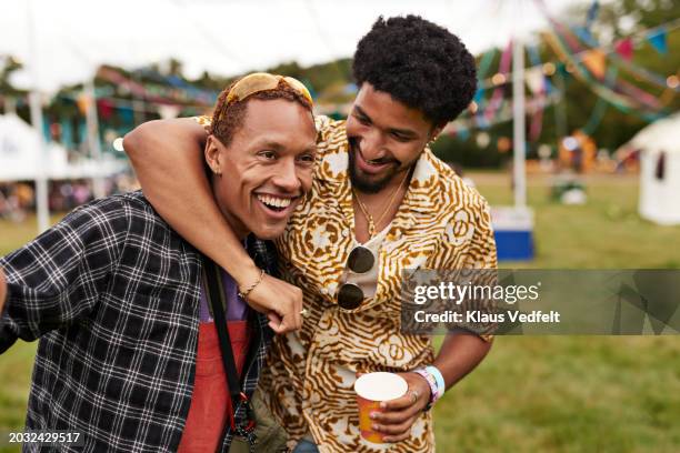 happy young man with arm around male friend - festivaleiro imagens e fotografias de stock