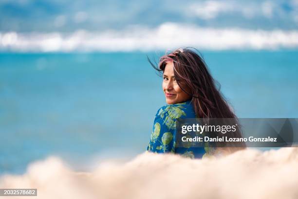 woman turning to smile at the camera sitting on the beach - breeze stockfoto's en -beelden