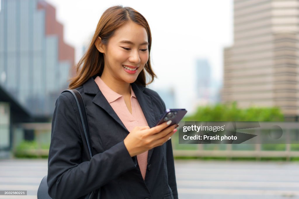 Asian woman using smartphone while walking in front of office building