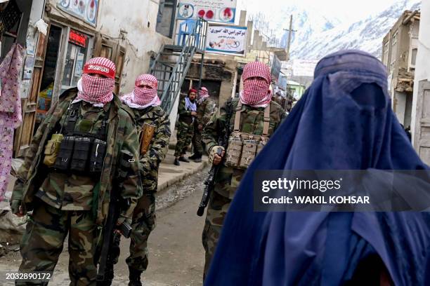 Taliban security personnel stand guard as an Afghan burqa-clad woman walks along a street at a market in the Baharak district of Badakhshan province...