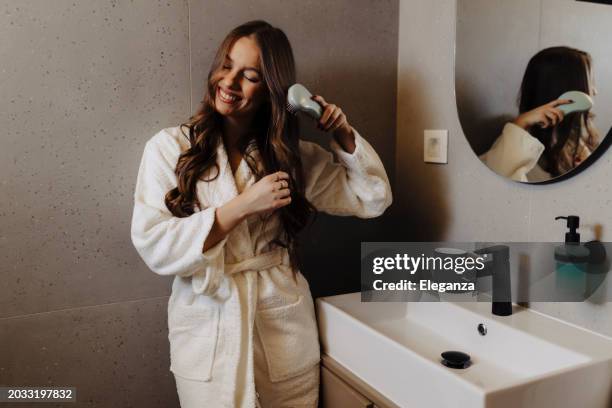 mujer peinando su hermoso cabello con cepillo mientras está de pie cerca del espejo en el baño - thick white women fotografías e imágenes de stock