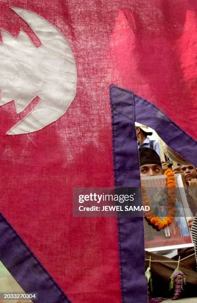 University student holding a portrait of the royal family draped in a garland can be seen through the national flag during a demonstration in...