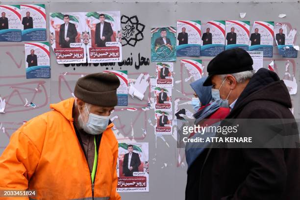 Pedestrians walk past a board bearing electoral campaign posters along a street in Abuzar, south of Tehran on February 26 ahead of next month's...