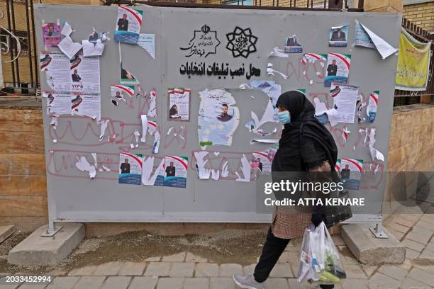 Pedestrian walks past a board bearing electoral campaign posters along a street in Abuzar, south of Tehran on February 26 ahead of next month's...