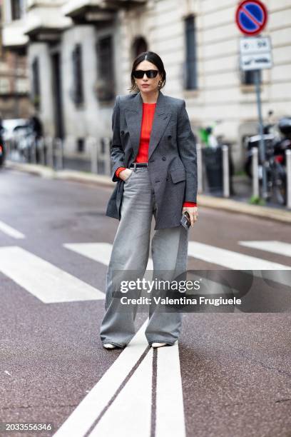 Guest is seen wearing black sunglasses, grey denim high waist wide leg trousers, a black belt, white shoes, a grey blazer and an orange sweater...