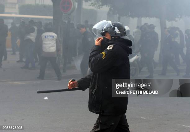 Tunisian policeman covers his face as riot police fire tear gas during a protest on Rome avenue in Tunis on January 18, 2011. Riot police fired tear...