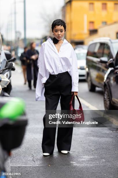 Guest is seen wearing a 3d fabric flower black chocker, a Rosso Ancora Gucci Jackie bag, a white oversized shirt, black high waist, wide leg trousers...