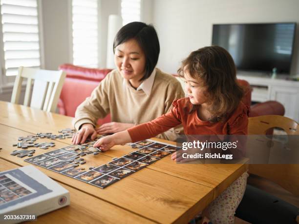 little girl and her mother doing a jigsaw puzzle - house puzzle stock pictures, royalty-free photos & images