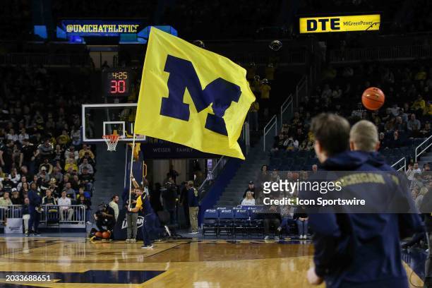 Michigan cheerleader runs with a large flag with the Michigan block "M" logo around the court before the start of a Big Ten Conference college...