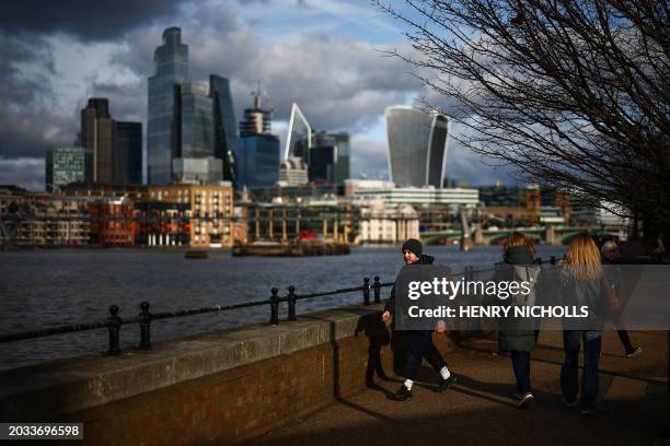 Members of the public walk alongside the River Thames in front of skyscrapers of the City of London including the 20 Fenchurch Street, commonly...