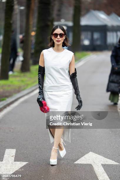 Heart Evangelista wears white sleeveless top, skirt, black gloves, heart shaped bag, platform shoes outside Sportmax during the Milan Fashion Week -...