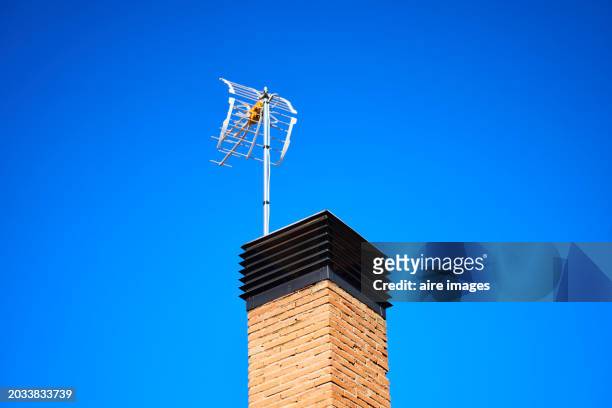 front view of a chimney on the roof of a house with a tv antenna, blue sky in the background. - new broadcasting house stock pictures, royalty-free photos & images
