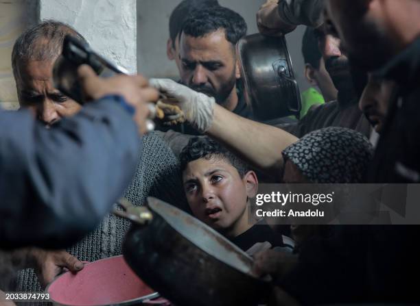 Palestinians with empty containers, pans wait to receive hot food distributed by charitables and charity organization in Gaza City, Gaza on February...