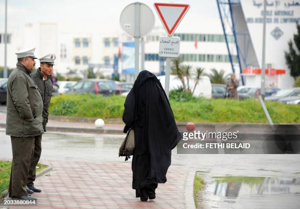 Student wearing a niqab walks by police before entering the University of Manouba's arts faculty outside Tunis on January 24, 2012 to take exams....