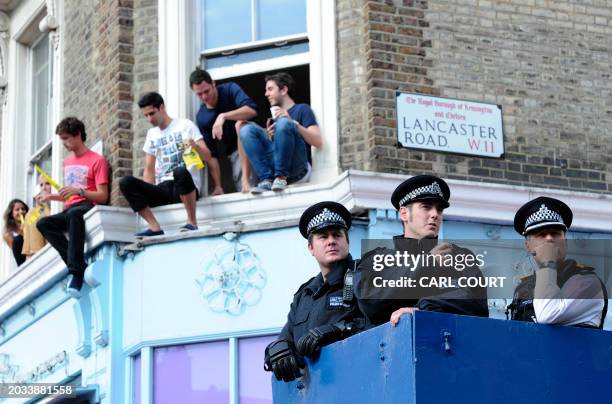 Police officers stand guard as spectators look the Notting Hill Carnival children's day from their windows, in London on August 28, 2011. The two-day...