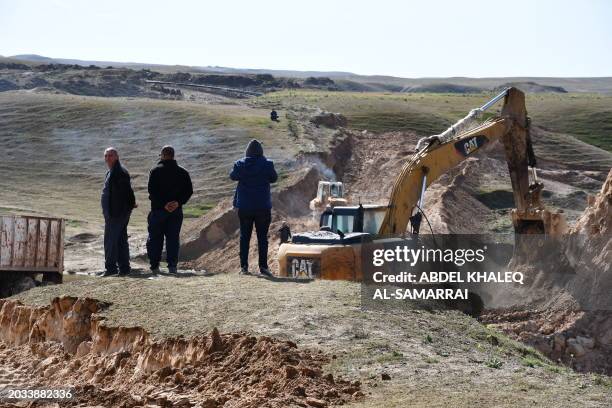 Iraqi farmers watch as excavators build up dirt barriers, a temporary measure to stem the flow of contaminated water onto farmland below, following...