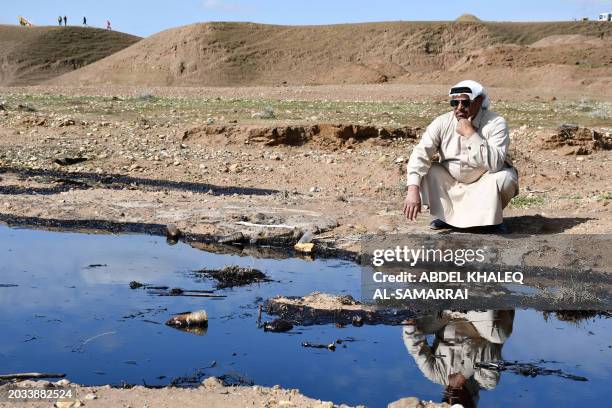 An Iraqi farmer squats and checks an oil spill into an agricultural land in the region of Hamrin, north of Tikrit, in the province of Salaheddin, on...
