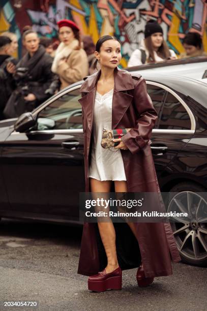 Guest wears a white silk dress, burgundy leather coat, and a Gucci bag outside Gucci during the Milan Fashion Week - Womenswear Fall/Winter 2024-2025...