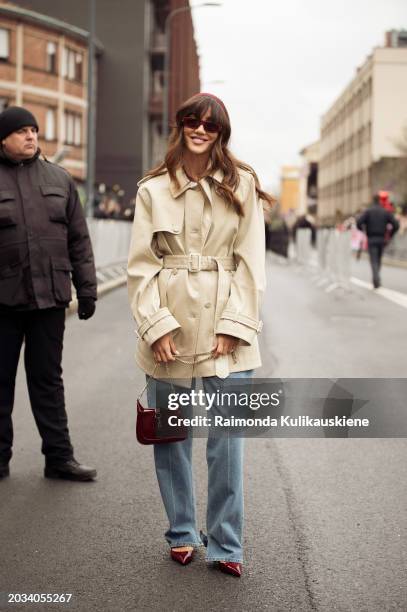 Tamara wears blue jeans, a beige trench coat, and a burgundy bag outside Gucci during the Milan Fashion Week - Womenswear Fall/Winter 2024-2025 on...