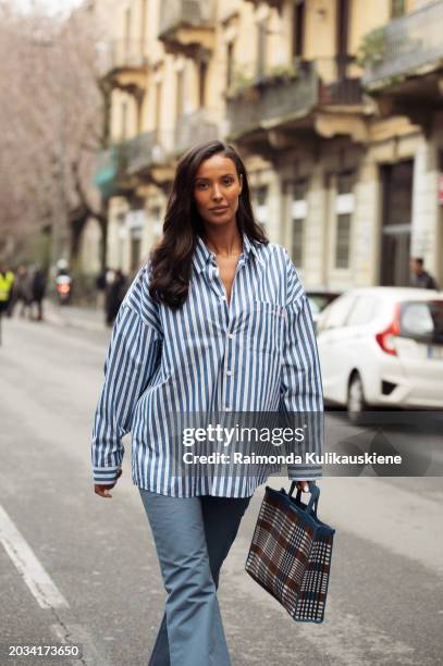 Guest wears, jeans, a white with blue stripes shirt, and a bag outside Marni during the Milan Fashion Week - Womenswear Fall/Winter 2024-2025 on...