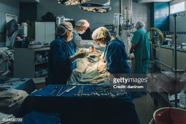 wide shot of the operating room with the surgical team operating. - suturing stock pictures, royalty-free photos & images