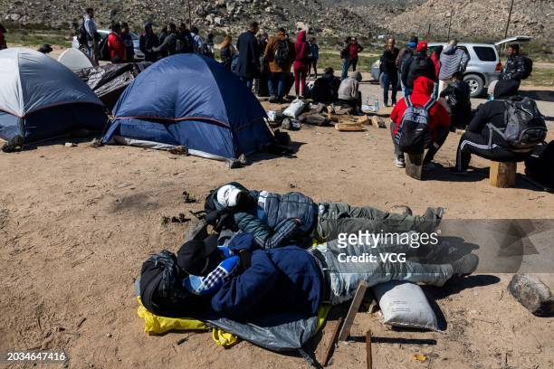 Migrants wait to be processed by the U.S. Border Patrol after crossing from Mexico at a makeshift camp next to the US border wall on February 23,...