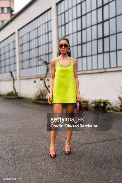 Camila Coelho wears sunglasses, a golden earrings, a neon yellow low neck sleeveless mini dress , a burgundy leather Gucci bag, shiny leather pointed...