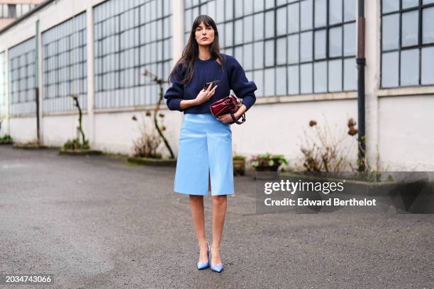 Leia Sfez wears a dark blue ribbed knitted wool pullover with puff sleeves, a burgundy leather bag, a pastel pale slit skirt in leather , pointed...